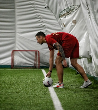 A footballer in a red kit places the ball on the line during an indoor training session.