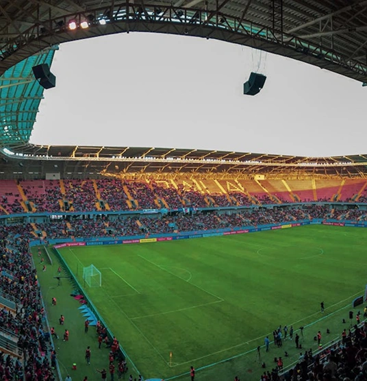 Panoramic view of a football stadium filled with supporters during a match, under a massive roof.